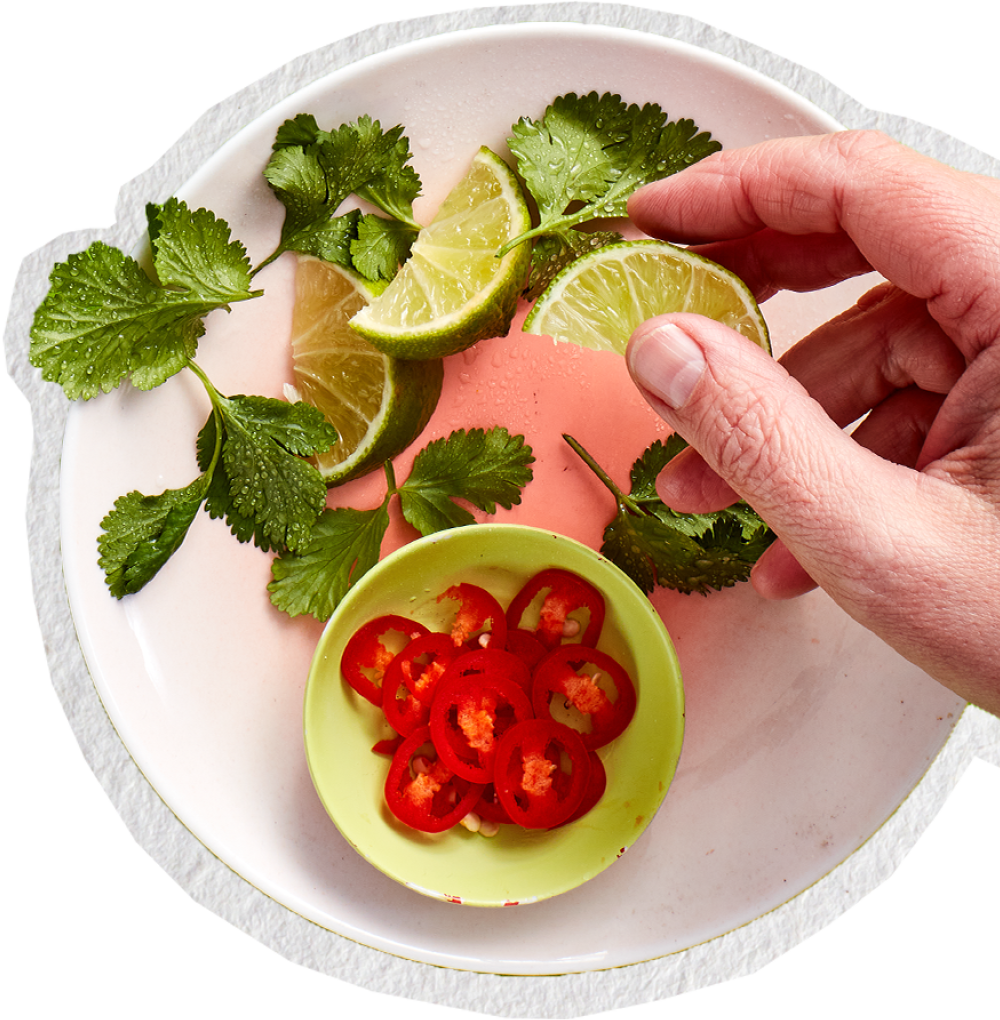 Hand holding lime wedges with fresh coriander and sliced red chilli