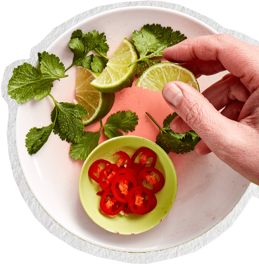 Hand holding lime wedges with fresh coriander and sliced red chilli